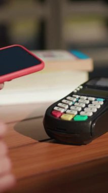 Ödeme terminali ahşap bir masanın üzerinde, kitaplarla çevrili, modern mali işlemleri vurguluyor..