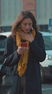 Genç bir kadın dışarıdayken akıllı telefonunu kontrol ediyor. Etrafı hareketli arabalar ve hareketli bir şehir manzarasıyla çevrili.