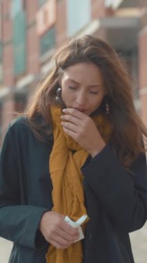 Siyah ceketli, sarı eşarplı, açık havada duran düşünceli bir kadın. Yüzündeki ifade derin düşünceleri yansıtıyor..