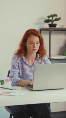 Videoda masasında tefekküre dalmış, çizgili gömlek giyen ve dizüstü bilgisayarına odaklanmış, iç gözlem gösteren kızıl saçlı bir kadın görülüyor.