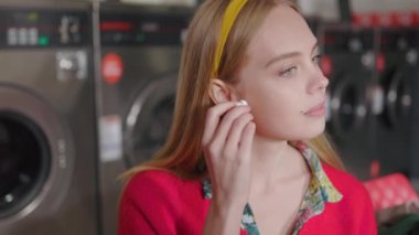 Portre, çamaşır makinesinin yanında oturan ve kulaklıkla müzik dinleyen güzel sarışın bir kadına ait. Çamaşır odası ev işi. Yavaş çekim