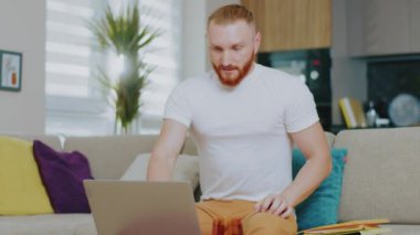 Kızgın genç yakışıklı adam kanepede otururken dizüstü bilgisayar kullanıyor. Çay iç. Evde çalış. İnternet teknolojisi. Karantina zamanı. Kapat..