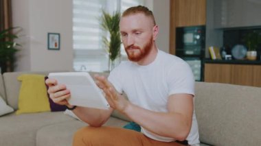 Tablet bilgisayar kullanan yakışıklı adamın yüzünü kapat. Odaklandım. Evdeki kanepede oturmak. Çevrimiçi teknoloji cihazı iletişim karantinası. Yavaş çekim