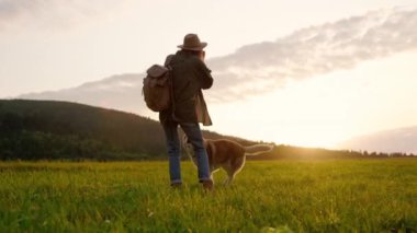 Güzel ve sakin bir günbatımı sahnesi neşeli bir kadın ve sevgili köpeğini doğanın tadını çıkarırken yakalıyor.