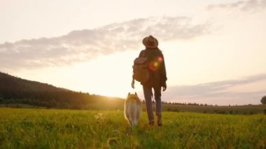 Bir kadın, güzel bir gün batımını izlerken sevgili köpeğiyle huzurlu bir tarlada yürümekten zevk alır.