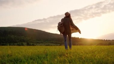 Bir kadın gün batımında güzel bir güneşli alanda sırtında bir çantayla yürürken doğada neşe bulur.