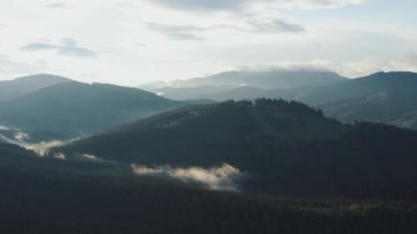 Sis ve yumuşak ışıklandırmanın yer aldığı sakin ve huzurlu bir dağ manzarası, doğal temalı projeler için ideal.