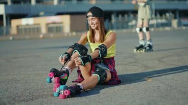 Gün ışığında genç bir kadın yerde oturuyor ve patenleri yerleştiriyor. Gülümsüyor. Yazın mutlu bir cadde.