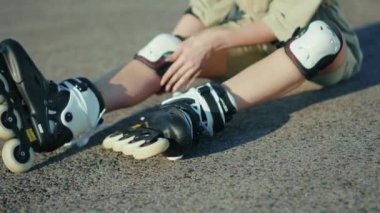 Kapalı yerde oturan genç bir kadın yaz aylarında gülümseyen caddelerde paten kayarken ağır çekimde patenler sürüyor.