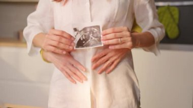 Birbirine aşık iki kadının ultrason fotoğrafını çekmesi ve mutfakta karnına dokunması.