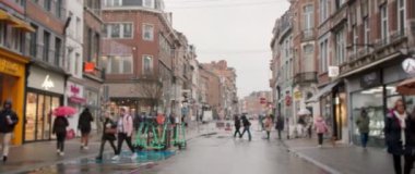 Yağmurlu bir günde çok sayıda yaya ve elektrikli scooterla dolu hareketli ve hareketli bir sokak sahnesi.