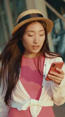 Havalı bir hasır şapka ve sıradan bir kıyafet giyen genç bir kadın, açık havada akıllı telefonuna tamamen dalmış durumda.