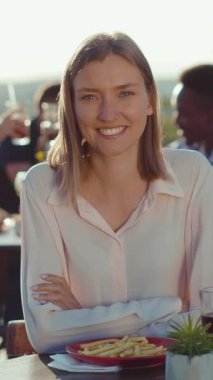 Neşeli bir kadın dışarıda güneşli bir yemek salonunda oturuyor, lezzetli kızartmaların tadını çıkarıyor ve son derece eğleniyor.