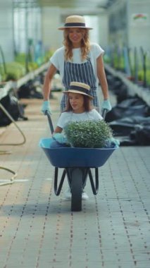 Neşeli bir yetişkin, mutlu bir çocukla birlikte bitkilerle dolu bir el arabası kullanarak bahçe işlerinden zevk alıyor.