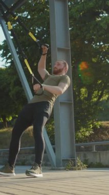 Kendini adamış bir fitness meraklısı, canlı bir açık hava ortamında TRX süspansiyon eğitimiyle aktif olarak meşgul.