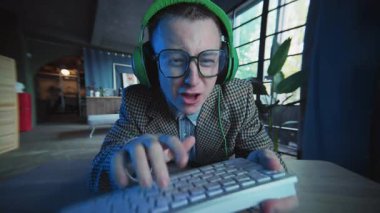 Gözlüklü ve kulaklıklı aktif adam klavyede bilgisayar kullanıyor. Gergin hissediyor. Erkek bakıyor. Ofis ya da daire