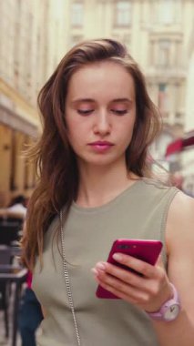 Genç bir kadın, hareketli bir şehrin hareketli sokaklarını keşfederken tesadüfen akıllı telefonunu kullanıyor.