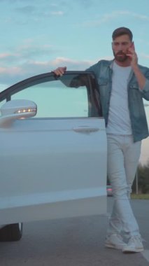 Şık bir genç adam güzel bulutlu bir gökyüzünün altında parlak beyaz bir arabayla eğlenceli bir etkileşimden hoşlanır.