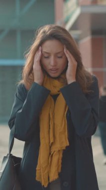 Bir kadın, şık bir şekilde sarı bir eşarpla süslenmiş canlı bir şehir ortamında düşünceli bir şekilde durmak için bir dakikasını ayırır.