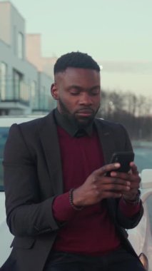 Çok şık giyinmiş bir adam şık bir şehir ortamında açık havada akıllı telefonunu kullanıyor.