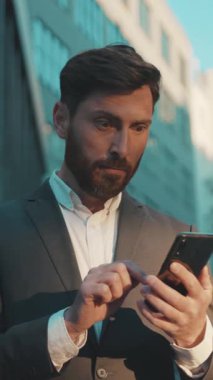 Profesyonel takım elbiseli bir adam modern bir şehirde açık havada akıllı telefonuyla meşgul oluyor.