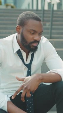 Düşünceli bir adam dışarıda oturur, beyaz bir gömlek ve kravat giyer, düşüncelere dalmıştır.