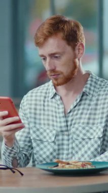 Bu videoda, bir adam bir masada oturuyor, cep telefonuna bakarken düşüncelere dalmış. Önünde bir tabak yemek dikkat dağıtıcı bir ana işaret ediyor.