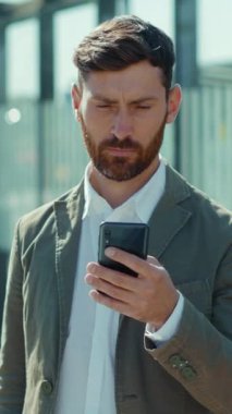 Takım elbiseli bir adam videoda cep telefonunu kullanıyor. Memnuniyetle gülümsüyor. Pozitif ve başarılı bir deneyim öneriyor.