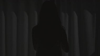 Kadın dışarıdaki güzel manzarayı görmek için pencere perdelerini açıyor. Mutlu tasasız kız otel odasından tropikal güneş ışığının tadını çıkarıyor..