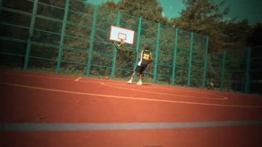 Yetenekli bir basketbolcu, verimli bir yeşilliğin kucakladığı canlı bir sahada atış talimine zaman ayırıyor.