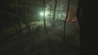 Askeri üniformalı iki donanımlı adamın gece yarısı taktik harekât sırasında ormanda silah taşırken insansız hava aracı görüntüleri. Araca atlayan asker. Savunma, savaş konsepti