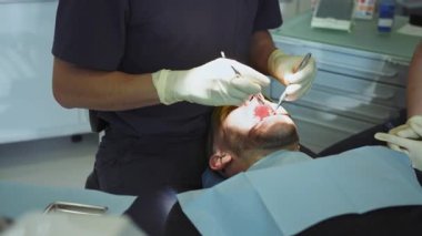 Dişleri tedavi eden bir adam. Eller dişçi ve asistanlar diş aletini tutuyor. Hydience ve sağlıklı. Modern klinik