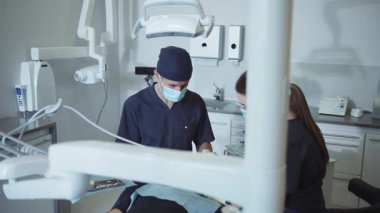 Tıbbi maskeli dişçiler ve asistanlar diş hastalarını tedavi eden bir diş aleti tutuyorlar. Hydience ve sağlıklı. Modern klinik