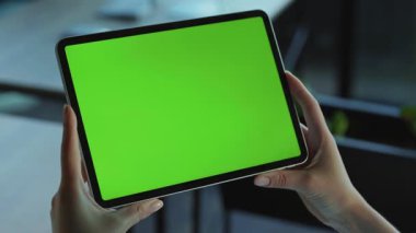 Elinde yeşil ekranlı tablet tutan kadın ofis çalışanının elleri. Aletin yatay görüntüsü. Kafkasyalı genç bir kadın etrafı kolaçan ediyor. Dokunmatik ekran. Modern teknolojiler. Arka plan bulanık. İnsanlar, insanlar