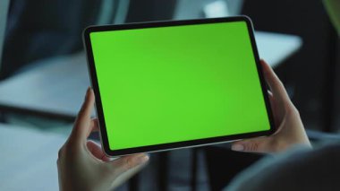 Yeşil ekranlı tablet kullanan beyaz bir kadının elleri görünüyor. Ofiste elinde alet tutan bir kız resmi. İş yerinin bulanık arkaplanı. Kapalı