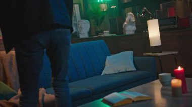 Kanepede oturup akıllı telefon alan mutlu, çekici, beyaz bir adamın görüntüsü. Gülümseyen adam ekrandaki cihaza bakıyor ve sohbet ediyor. Randevu uygulamaları. İçeride. Modern iç mimari