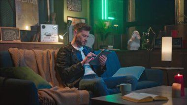 Çekici genç adamın online alışverişinin yatay görüntüsü. Sakallı adamın tablet ekranına dokunması, internette sörf yapması. Arkaplanda yeşil neon ışığı