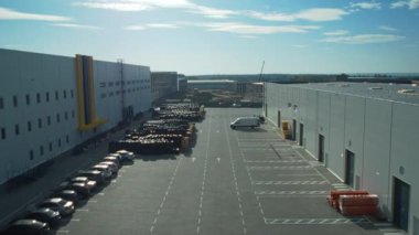 Modern çağdaş bir depo, temiz mavi gökyüzünün altında, teslimat araçları için organize park yeri barındırıyor.