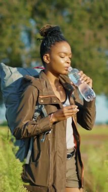 Genç bir kadın, güzel bir patikada sırt çantasıyla yürüyüp, suyunu yudumlarken, serinletici bir anın tadını çıkarıyor.