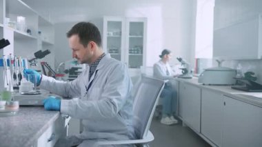 Profesyonel biyoteknoloji bilim adamlarından oluşan bir ekiple aşı geliştiren bir tıp laboratuvarı. Adam deney yapıyor ve kadın biyokimyacı mikroskopta çalışıyor. İçeride. Gündüz vakti. Yenilik