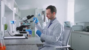 Erkek bilim adamının elinde örnekler tutarken ve mikroskoptan bakarken görüntüsü. Laboratuvardaki modern ekipmanları kullanan laboratuvar önlüklü genç adam. Deneme. Bilim ve tıp konsepti. Sağlık Hizmetleri