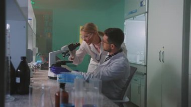Modern tıbbi araştırma laboratuvarında çalışan erkek ve kadın bilim adamları. Bilim laboratuarında mikroskoptan bakan Kafkas meslektaşlarının fotoğrafı. İyi akşamlar. Kapalı