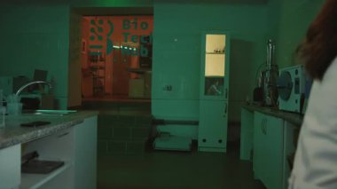 Genç kadın bilim adamının laboratuvar odasında modern ekipmanları kullanırken iş yerinde oturduğu ve örnek aldığı görüntüler. Akşam bilim laboratuarında çalışan kadın ve erkek. Kapalı