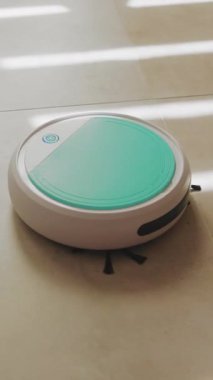 Modern beyaz ve yeşil bir robotik vakum fayanslarla döşenmiş bir zeminde ev temizliği ve bakımı için tasarım ve işlevselliğini vurguluyor.