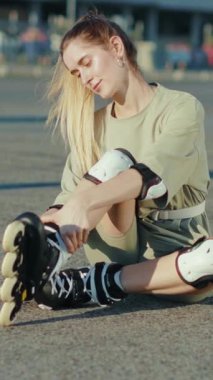 Neşeli bir kadın yerde oturuyor, patenlerini koruyucu dizliklerle bağlıyor, parkta kayak yapmak için heyecanlı.