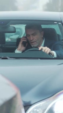 Düşünceli bir adam sisli bir caddede araba sürerken görülüyor, şehir yaşamını ve yansıma anlarını gösteriyor..