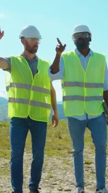 Güvenlik yelekleri ve kask giyen iki inşaat işçisi açık hava inşaatında çalışıyor.