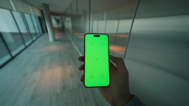 Yeşil ekranlı, el ele tutuşan ve dikey olarak telefonu kaydıran adamı kapat. Arka planda büyük pencereli modern alan. Akıllı telefondan yazıyorum.