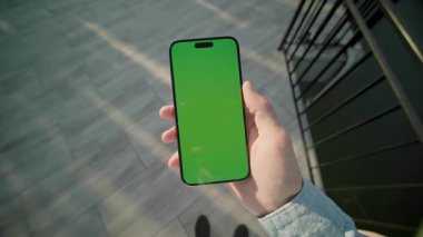 Güneş ışığı adamı yeşil ekran ile dikey olarak telefonu tutuyor ve kaydırıyor. Arka plandaki gölde. Akıllı telefondan yazıyorum.