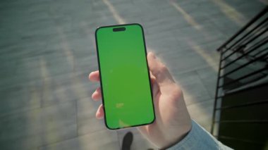 Yeşil ekran hareket ederken el ele tutuşan ve dikey olarak telefonu kaydıran adam. Arka plandaki gölde, güneş ışığında. Akıllı telefondan yazıyorum.